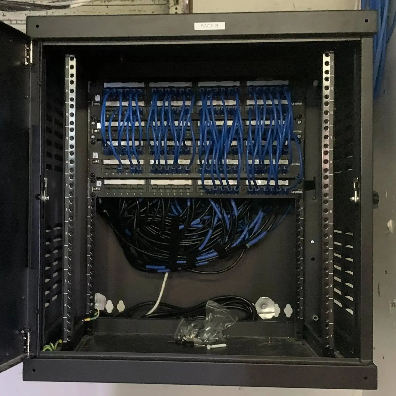 Wall-mounted network cabinet with blue patch cables and a cable management tray